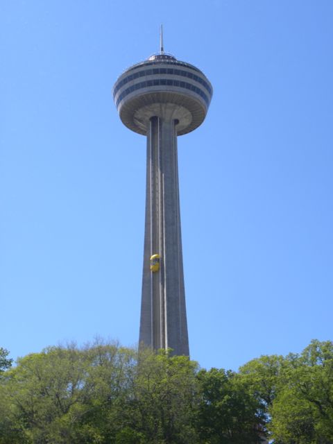 Tower with circular structure on top and yellow exterior pod elevator one-third the way up to the top