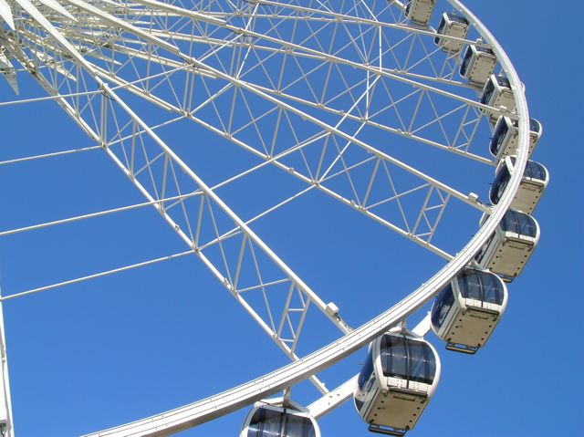 Section of metal ferris wheel with pods against a briliant blue sky