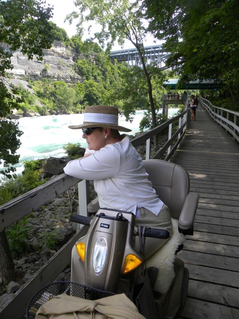 Linda on her scooter on a long wooden boardwalk beside the rapids